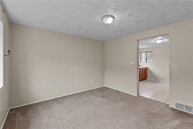 empty room featuring visible vents, light tile patterned flooring, light carpet, and a textured ceiling