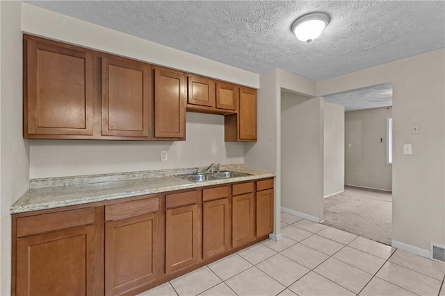 kitchen with visible vents, a sink, brown cabinets, light tile patterned flooring, and light carpet