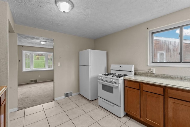 kitchen featuring visible vents, brown cabinetry, white appliances, and light countertops