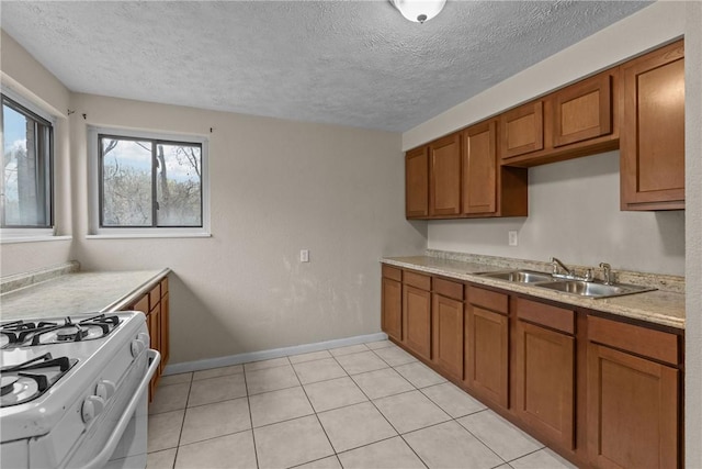 kitchen featuring white gas range oven, light countertops, a sink, brown cabinets, and baseboards