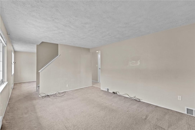 unfurnished living room with carpet, visible vents, and a textured ceiling