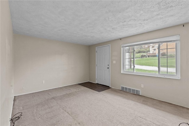 unfurnished room featuring a textured ceiling, carpet, and visible vents