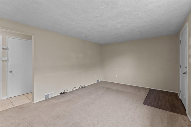 tiled spare room with visible vents, carpet flooring, and a textured ceiling