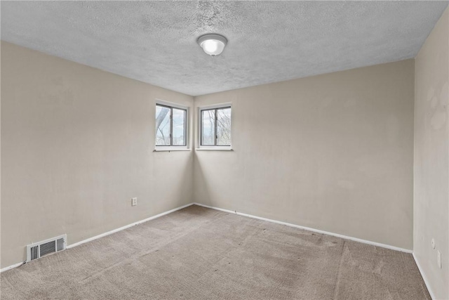 carpeted spare room featuring a textured ceiling, baseboards, and visible vents