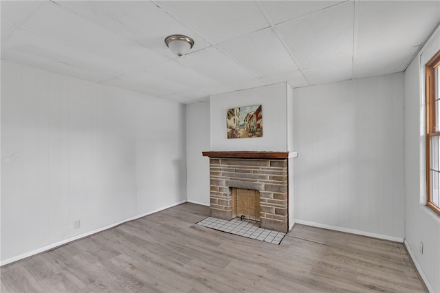 unfurnished living room featuring a stone fireplace, baseboards, and wood finished floors