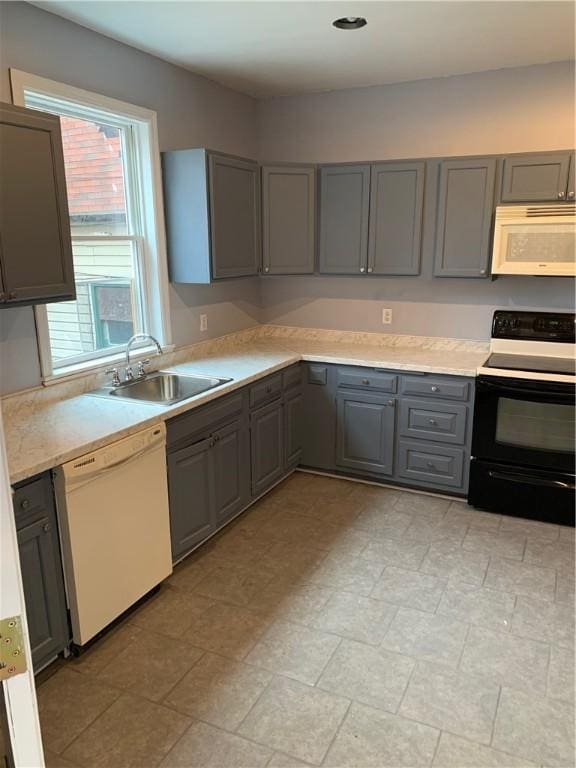 kitchen with a sink, gray cabinets, light countertops, and white appliances