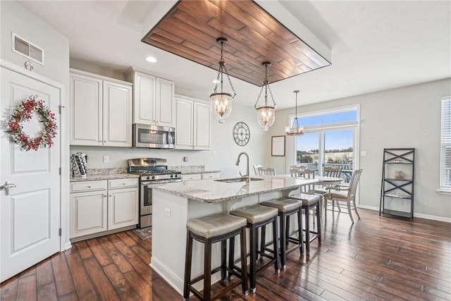 kitchen with a kitchen bar, visible vents, appliances with stainless steel finishes, a sink, and a center island with sink