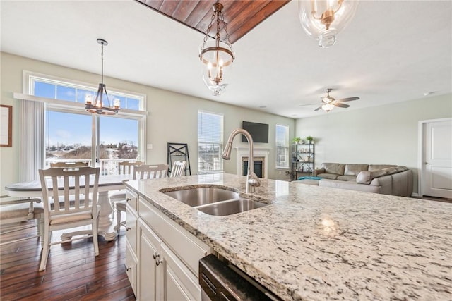 kitchen with a sink, decorative light fixtures, light stone counters, and dark wood finished floors