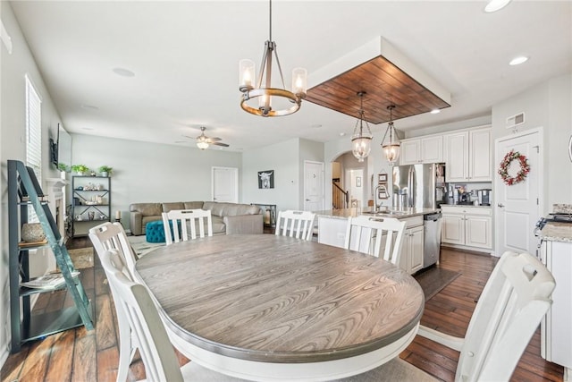 dining room with dark wood-type flooring, arched walkways, ceiling fan with notable chandelier, and visible vents