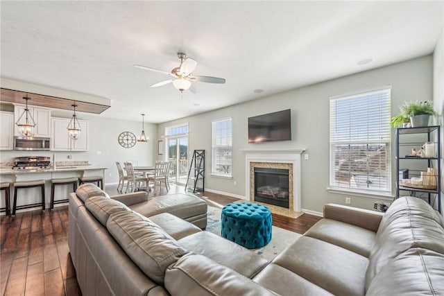 living area with a high end fireplace, ceiling fan, baseboards, and dark wood finished floors