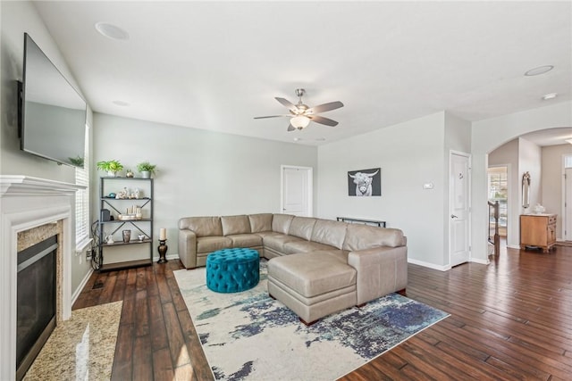 living room with ceiling fan, dark wood finished floors, arched walkways, a premium fireplace, and baseboards