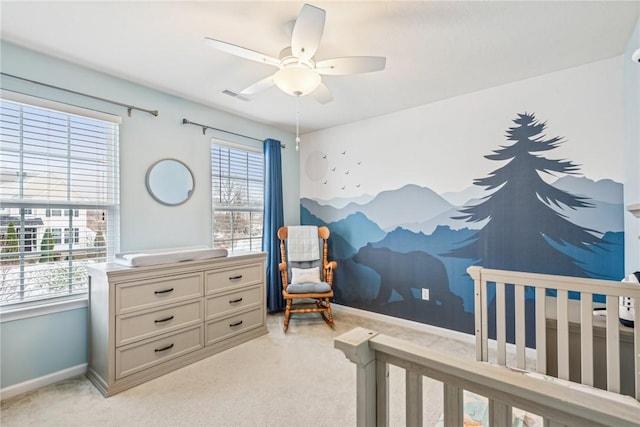 bedroom featuring visible vents, baseboards, a nursery area, ceiling fan, and light colored carpet