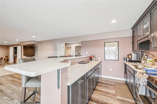 kitchen with a sink, light countertops, a breakfast bar, recessed lighting, and light wood finished floors
