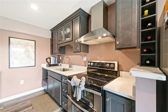 kitchen featuring light countertops, a sink, wall chimney range hood, and range with two ovens