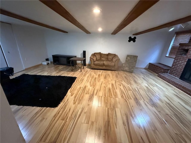 living area featuring a brick fireplace, beamed ceiling, and wood finished floors