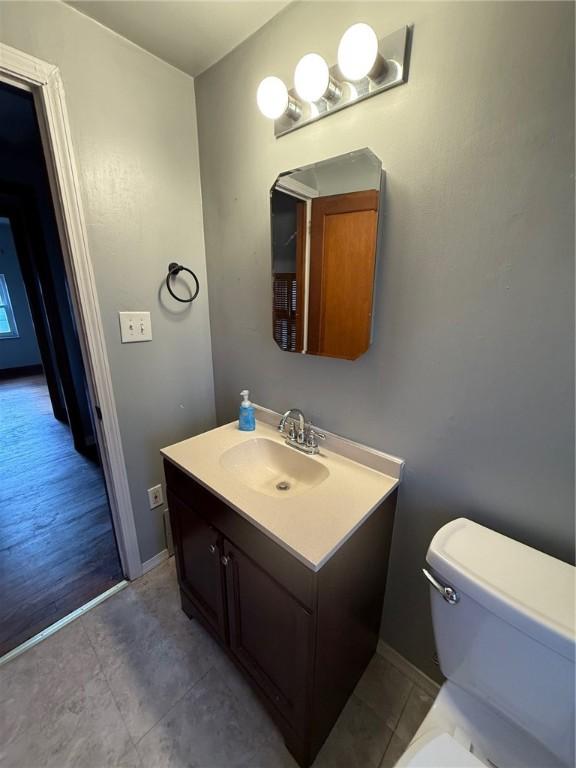 half bathroom featuring tile patterned flooring, vanity, baseboards, and toilet