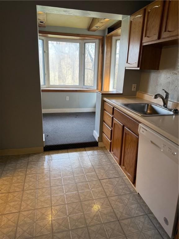 kitchen with baseboards, white dishwasher, a sink, light countertops, and light floors