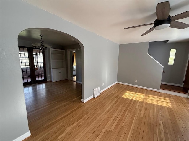 spare room featuring arched walkways, visible vents, hardwood / wood-style flooring, and baseboards