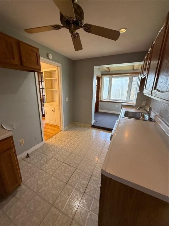 kitchen featuring a sink, a ceiling fan, baseboards, and light floors