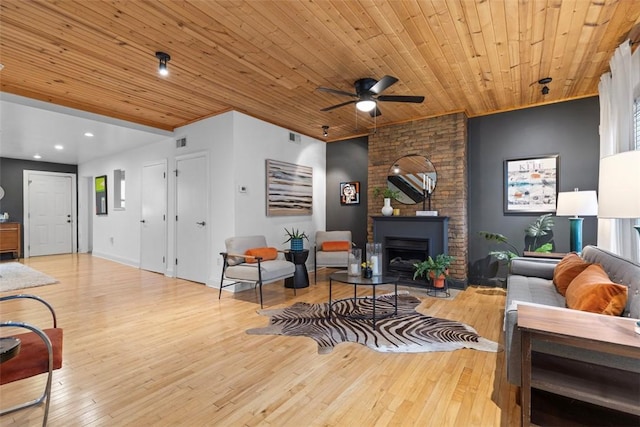 living area featuring visible vents, wooden ceiling, ceiling fan, wood finished floors, and a large fireplace