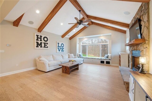 living room featuring baseboards, lofted ceiling with beams, a stone fireplace, light wood-type flooring, and a ceiling fan
