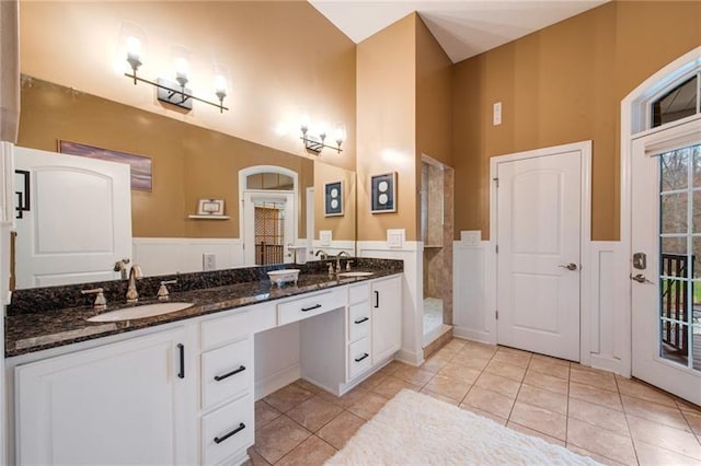 bathroom with a towering ceiling, a sink, double vanity, tile patterned flooring, and a tile shower