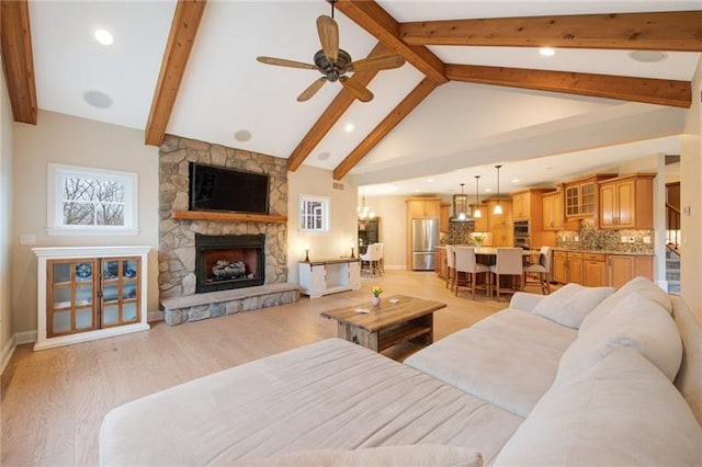 living room featuring baseboards, a stone fireplace, ceiling fan, light wood-type flooring, and beamed ceiling