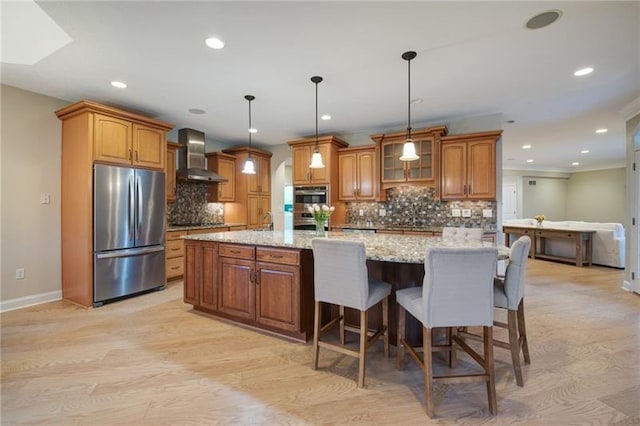 kitchen featuring brown cabinetry, appliances with stainless steel finishes, wall chimney exhaust hood, and baseboards