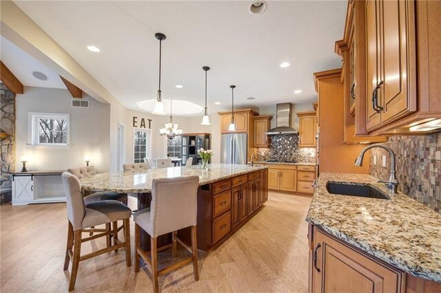 kitchen featuring freestanding refrigerator, wall chimney exhaust hood, tasteful backsplash, visible vents, and a sink