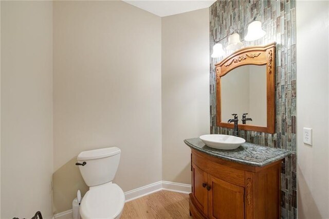 half bath featuring toilet, baseboards, vanity, and wood finished floors