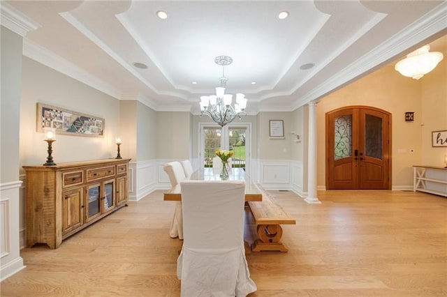 dining space with a notable chandelier, light wood-style floors, a tray ceiling, decorative columns, and a decorative wall