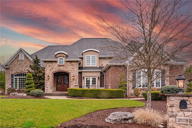 french provincial home with a yard, french doors, stone siding, and stucco siding