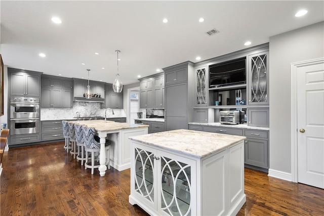 kitchen with gray cabinets, a center island with sink, visible vents, decorative backsplash, and appliances with stainless steel finishes