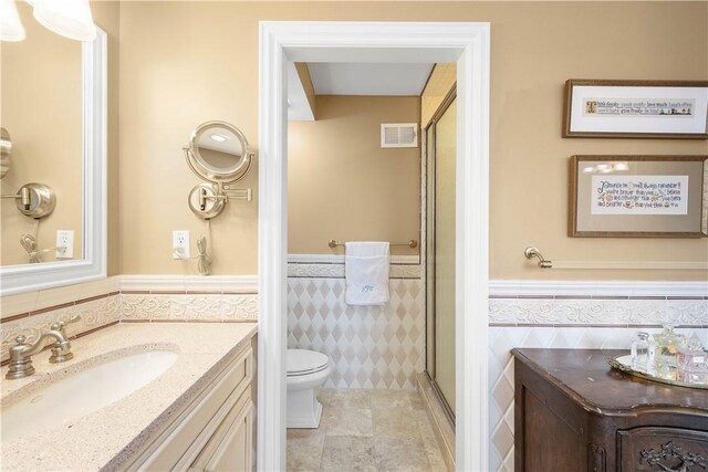 bathroom featuring a shower stall, vanity, visible vents, a wainscoted wall, and tile walls