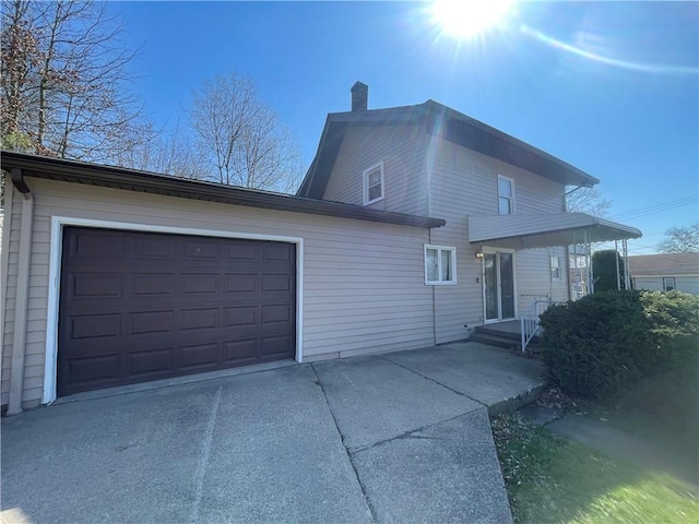 view of front facade featuring concrete driveway, a chimney, and an attached garage