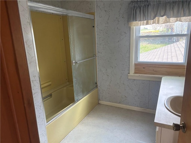 bathroom featuring combined bath / shower with glass door, vanity, baseboards, and wallpapered walls
