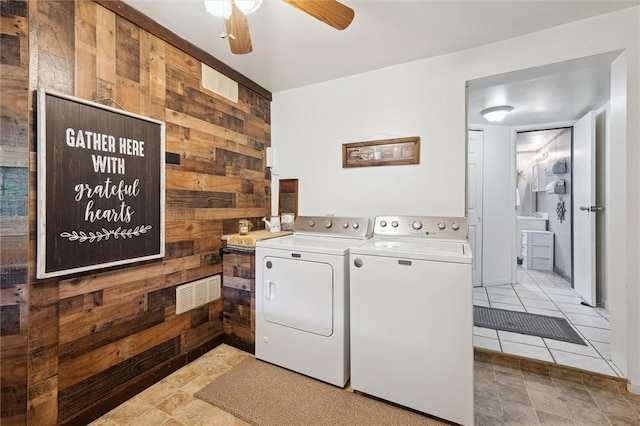 clothes washing area with wood walls, ceiling fan, washing machine and dryer, and laundry area