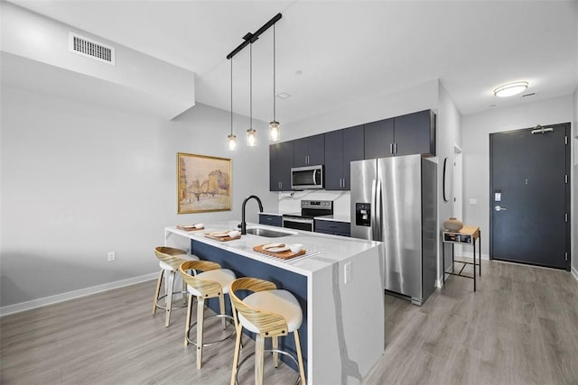 kitchen featuring light wood-style flooring, a sink, light countertops, stainless steel appliances, and a breakfast bar area