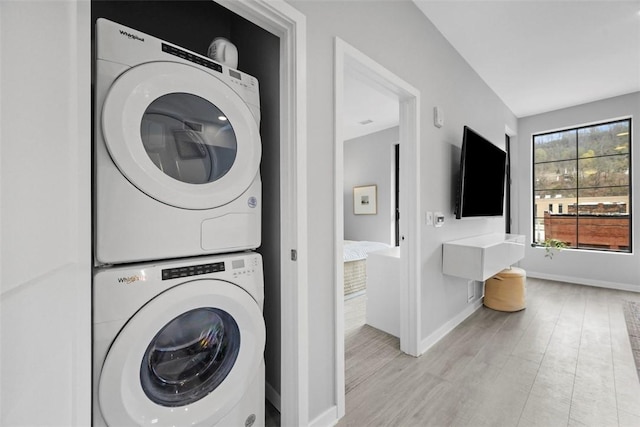 laundry room with laundry area, stacked washer and dryer, baseboards, and light wood-style floors
