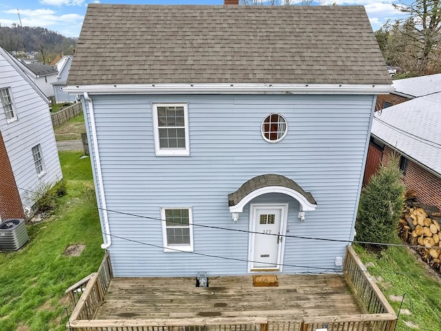 view of front of home with central air condition unit, a chimney, a front yard, fence, and a shingled roof
