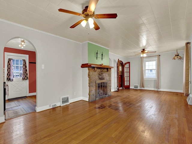 unfurnished living room with arched walkways, visible vents, a ceiling fan, and ornamental molding