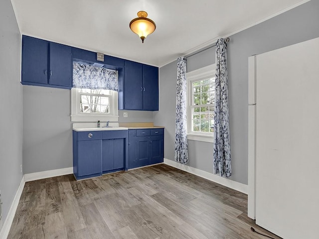 kitchen featuring baseboards, light countertops, light wood-type flooring, freestanding refrigerator, and blue cabinetry
