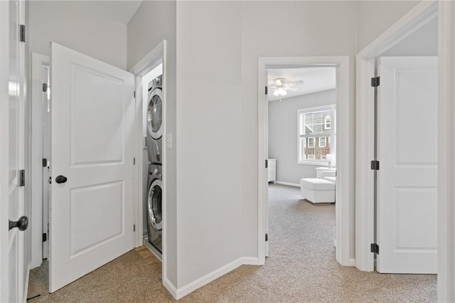 washroom with laundry area, ceiling fan, light carpet, baseboards, and stacked washer / drying machine