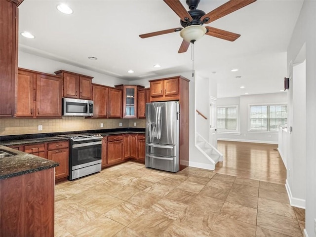 kitchen featuring glass insert cabinets, backsplash, a ceiling fan, brown cabinets, and stainless steel appliances