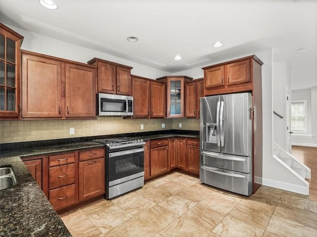 kitchen with tasteful backsplash, glass insert cabinets, appliances with stainless steel finishes, and dark stone countertops