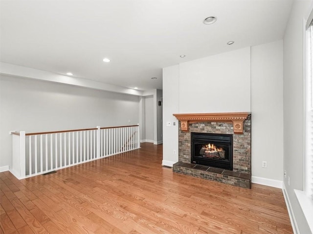 unfurnished living room with wood finished floors, a fireplace, baseboards, and recessed lighting