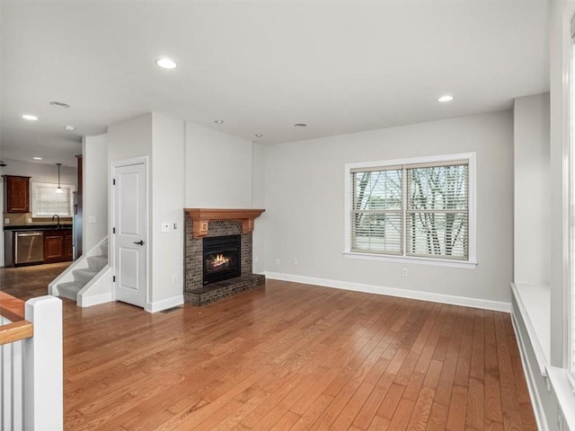 unfurnished living room featuring a fireplace, recessed lighting, a sink, baseboards, and hardwood / wood-style flooring