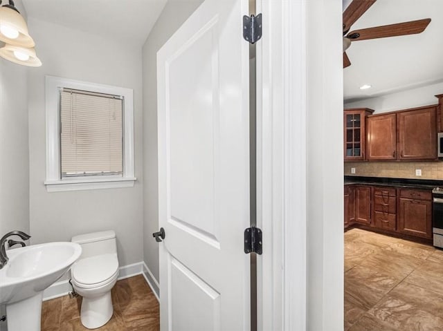 bathroom with baseboards, a sink, toilet, ceiling fan, and decorative backsplash