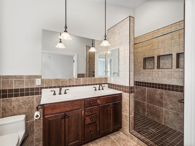 bathroom featuring toilet, double vanity, a sink, and tile walls