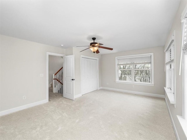 unfurnished bedroom with ceiling fan, a closet, light colored carpet, and baseboards